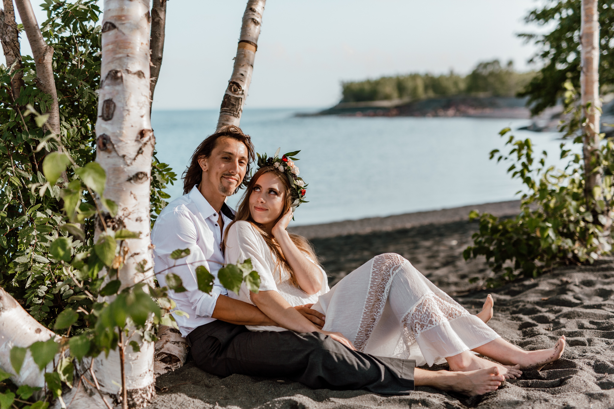 bride and groom leaning against a tree on the beach with groom looking at the camera and bride admiring her husband