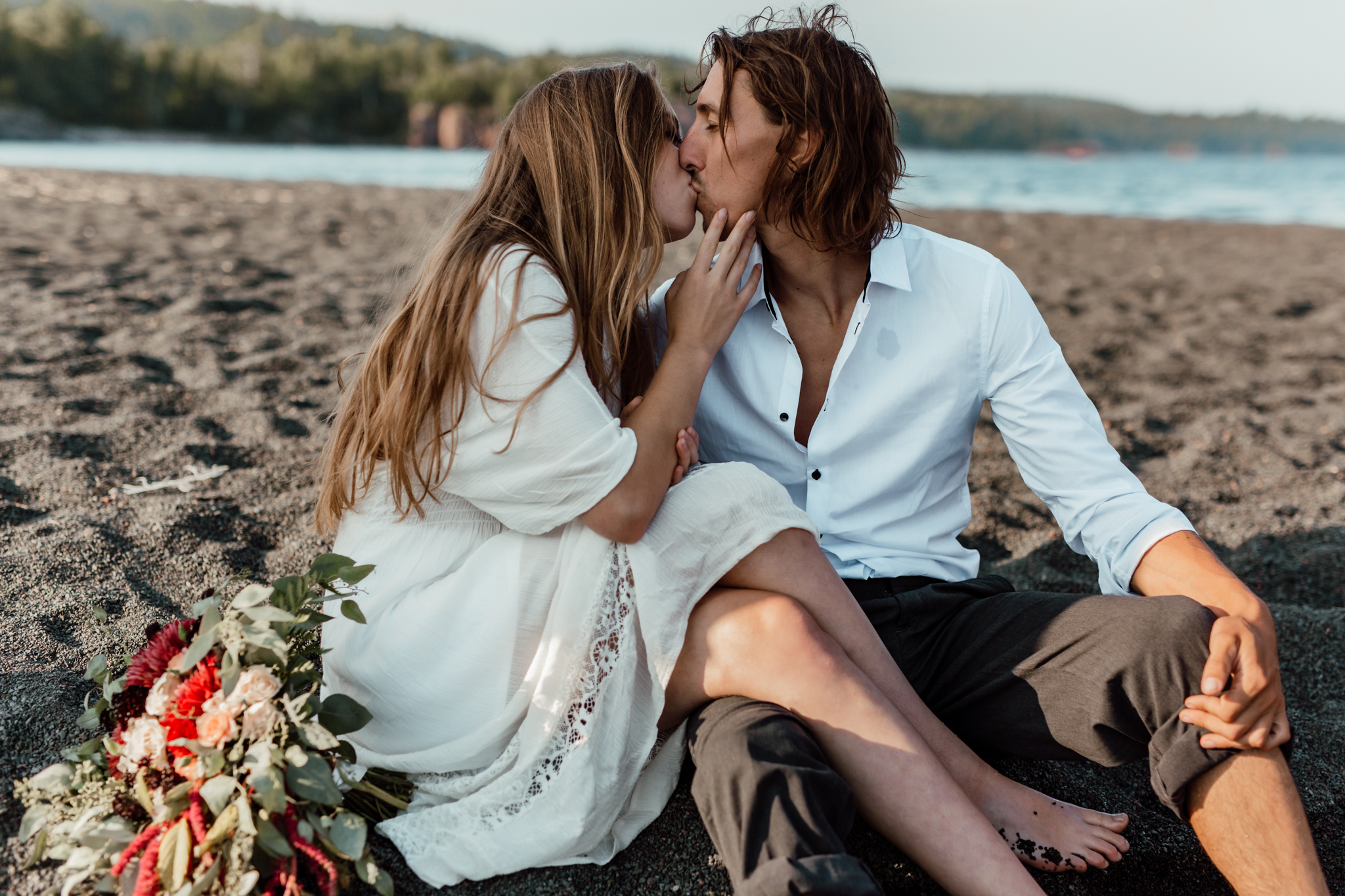 a shared kiss between bride and groom sitting on the beach 