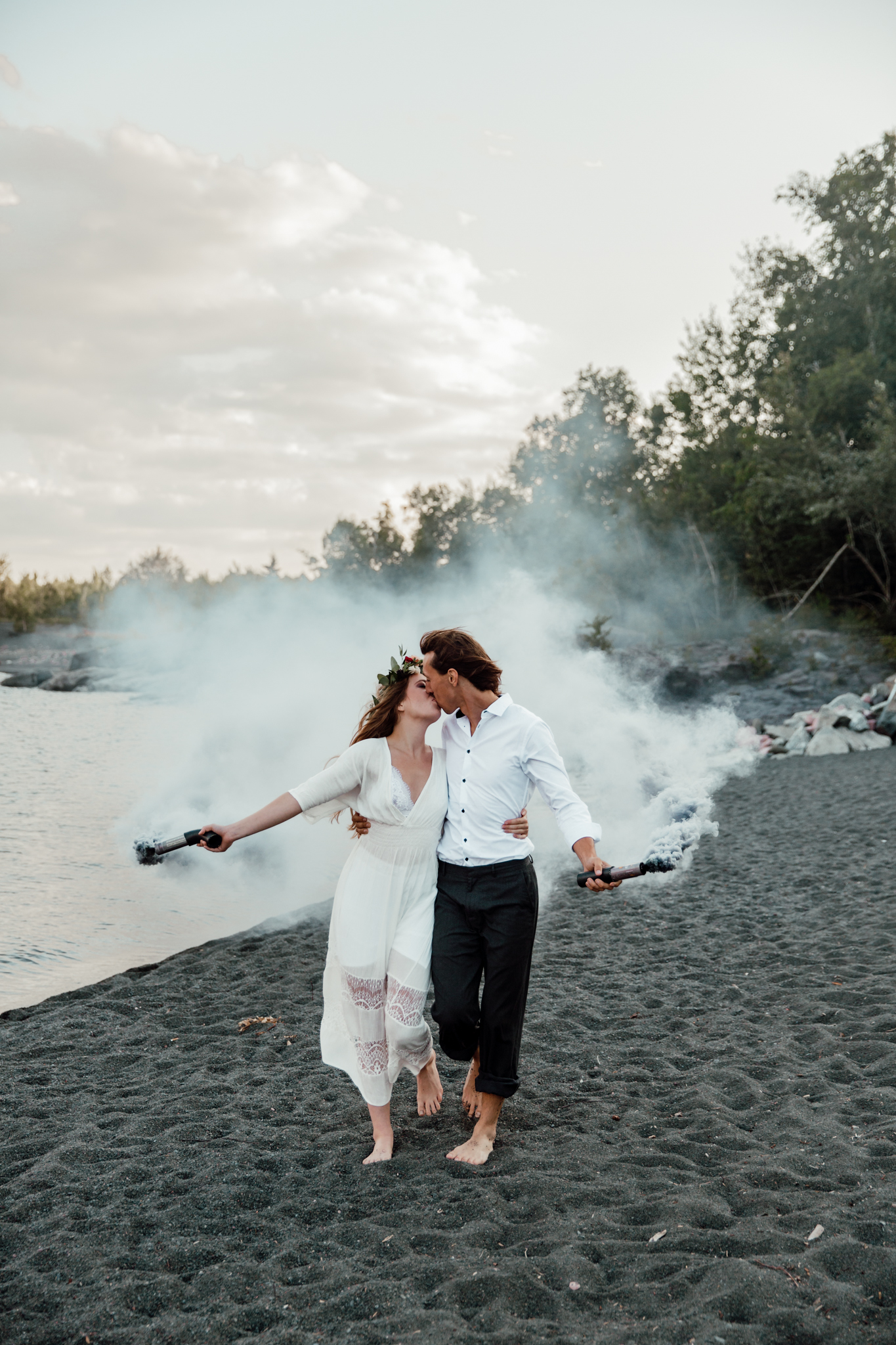 bride and groom walking on a black sand beach holding smoke bombs going in for a kiss