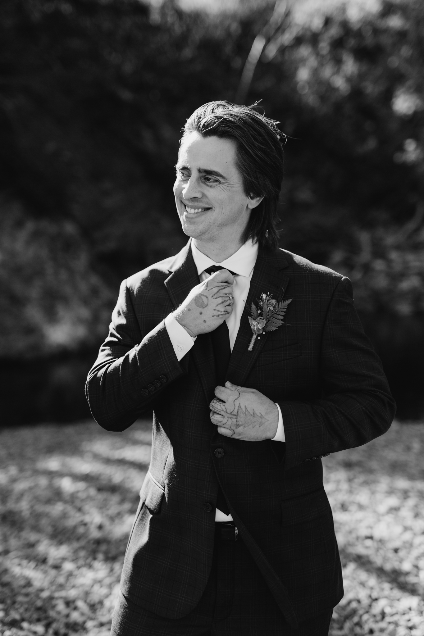 black and white portrait of groom looking off into the distance while fixing his tie 
