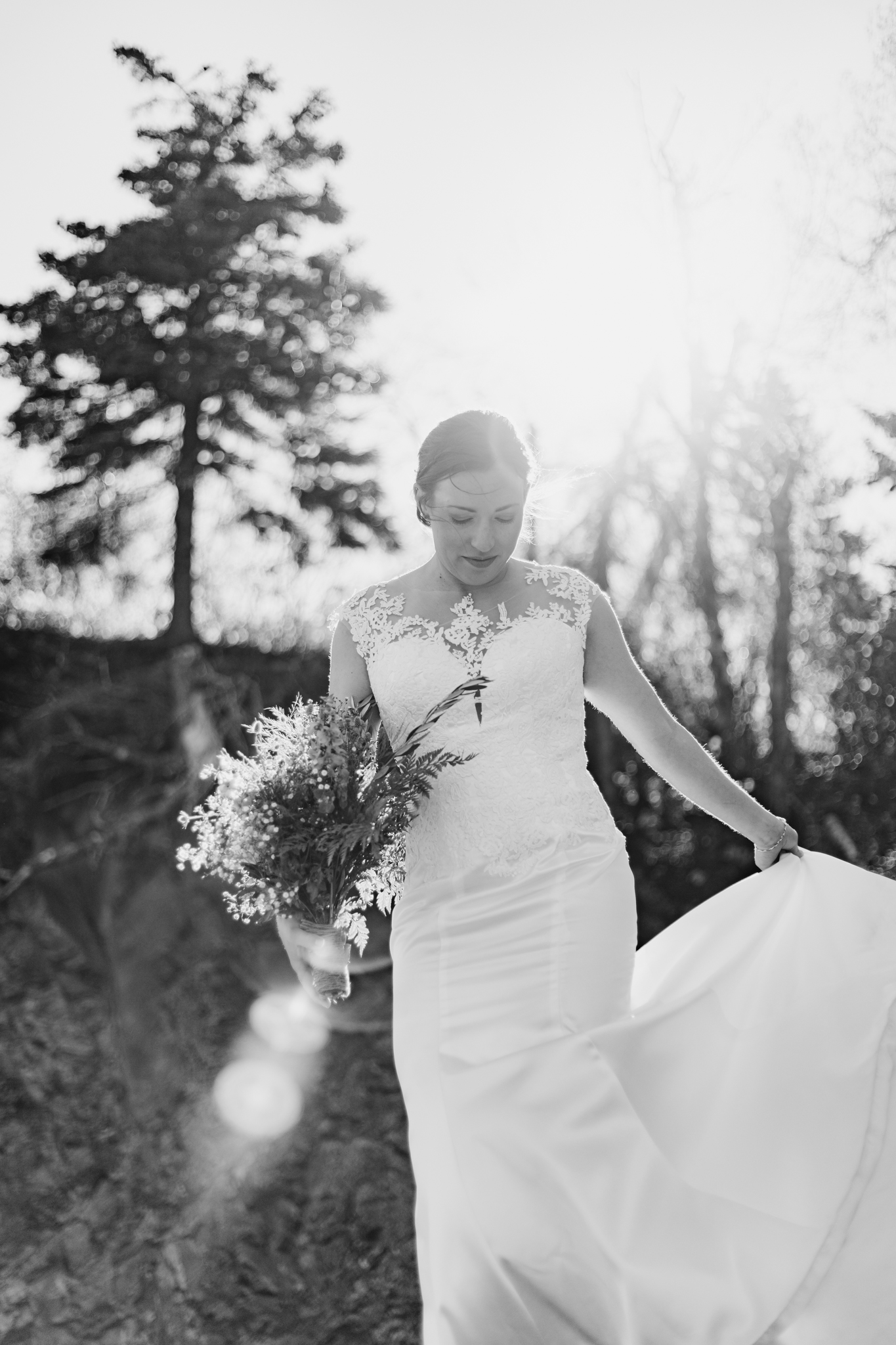 black and white portrait of bride moving the skirt of her dress with a sunflare 