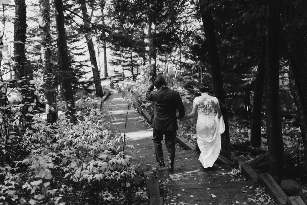 black and white image with bride and groom holding hands and walking along a hiking trail 