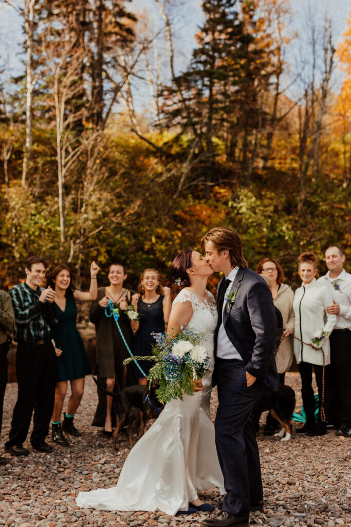 elopement kiss with family and dogs cheering in the back with lots of fall colors 