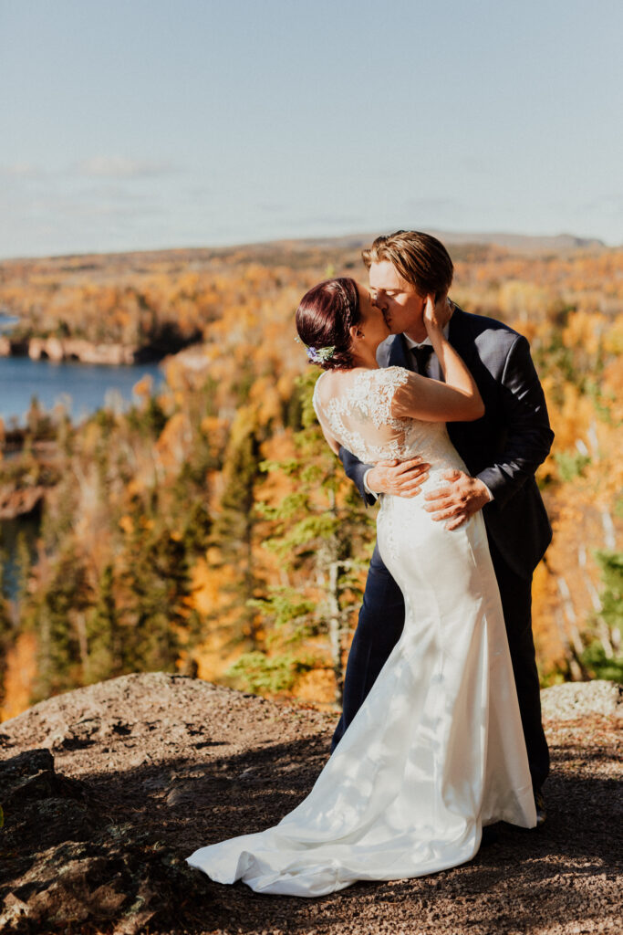 dip kiss elopement portrait with minnesota's shoreline behind them and fall colors in full effect 