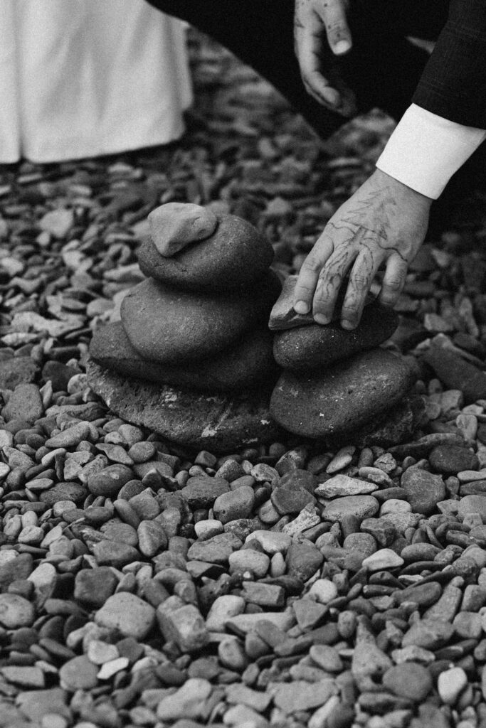 closeup detail shot of the elopement ceremony rock stack with grooms hand placing a stone