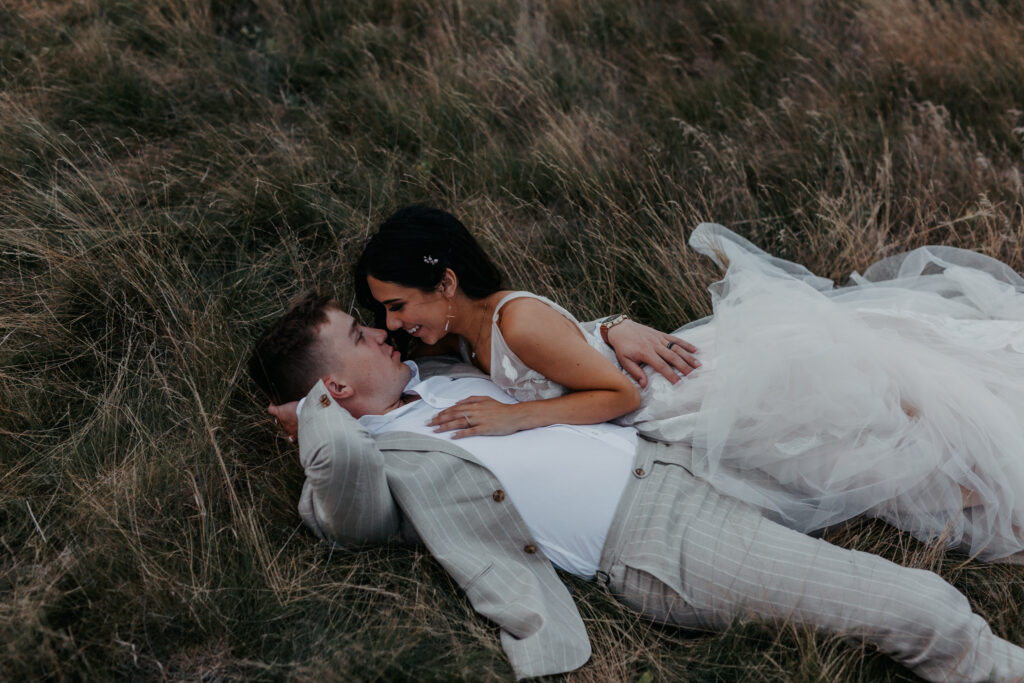 bride and groom laying in a field with her relaxing on his chest 