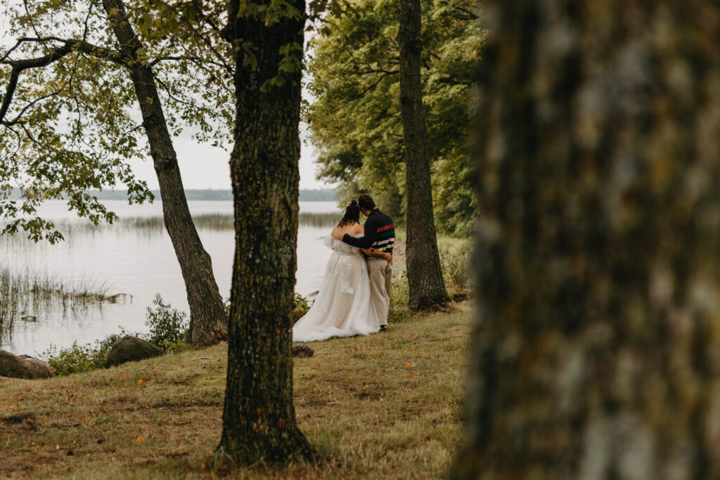 wedding couple holding each other looking off into the distance right next to a lake 