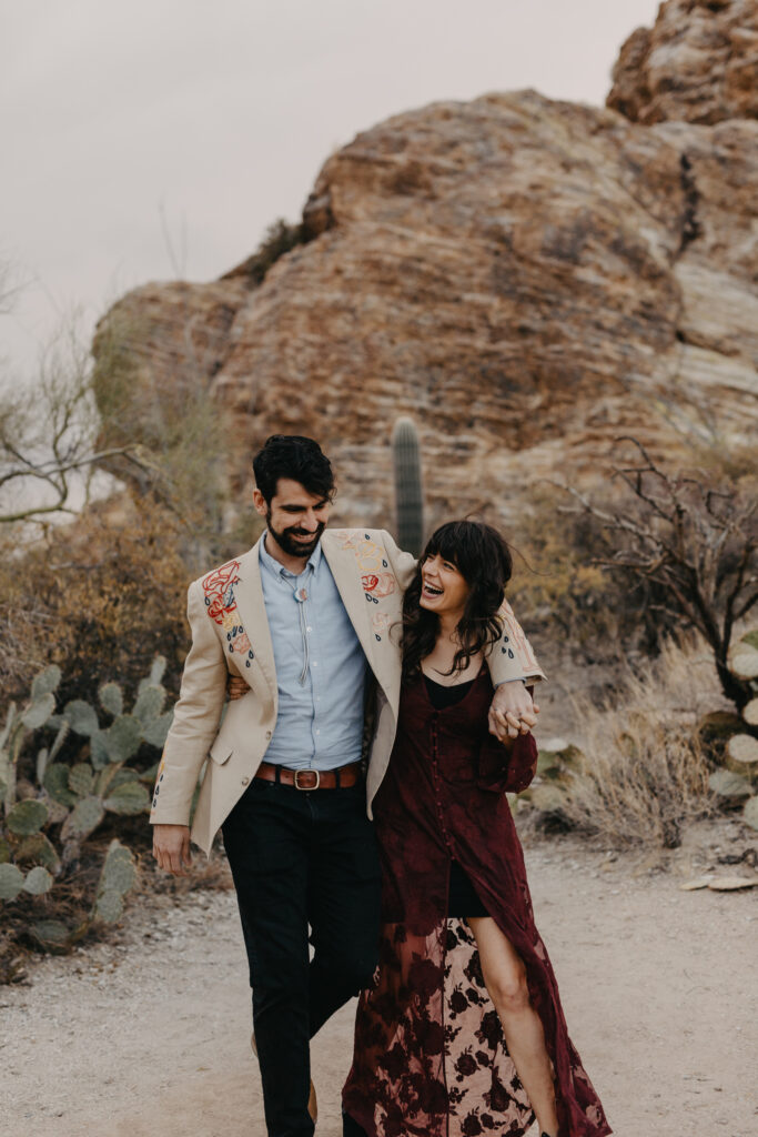 grooms arm is wrapped around the bride and they're laughing walking towards the camera with saguaro cacti behind them 