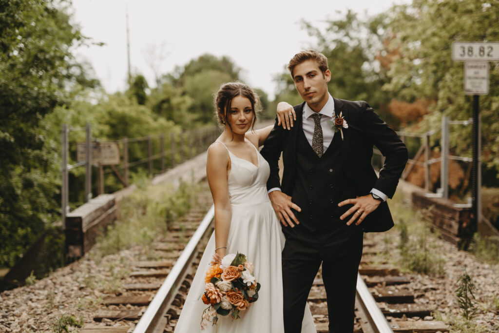 moody and editorial pose of bride and groom seriously looking at the camera on rail road tracks in minnesota 