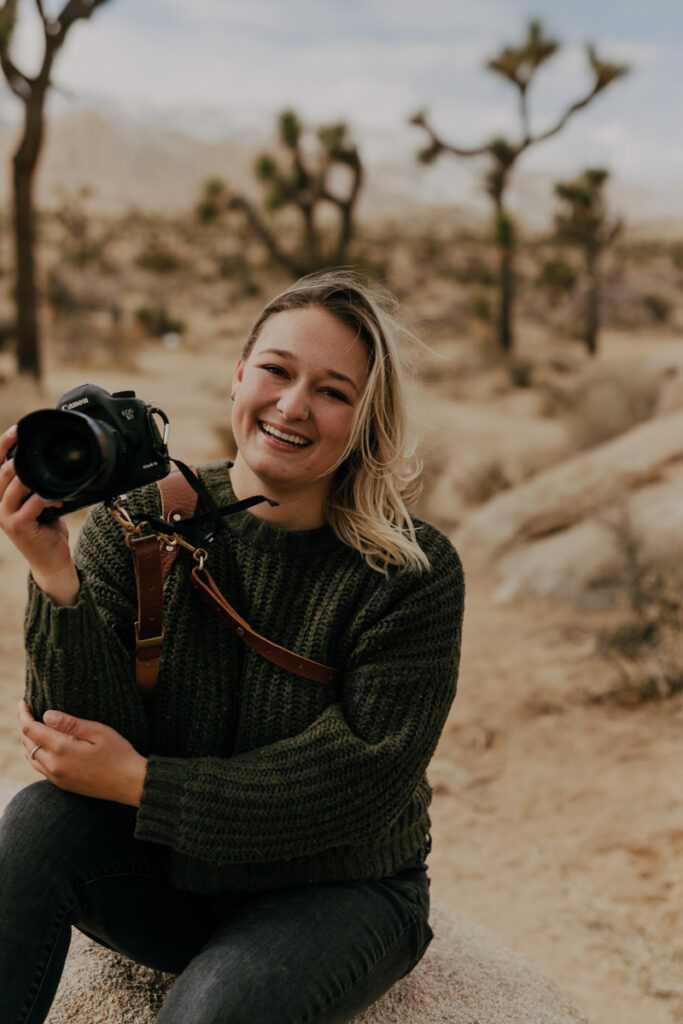 smiling picture of brianna kirk holding her camera for a headshot at joshua tree national park 
