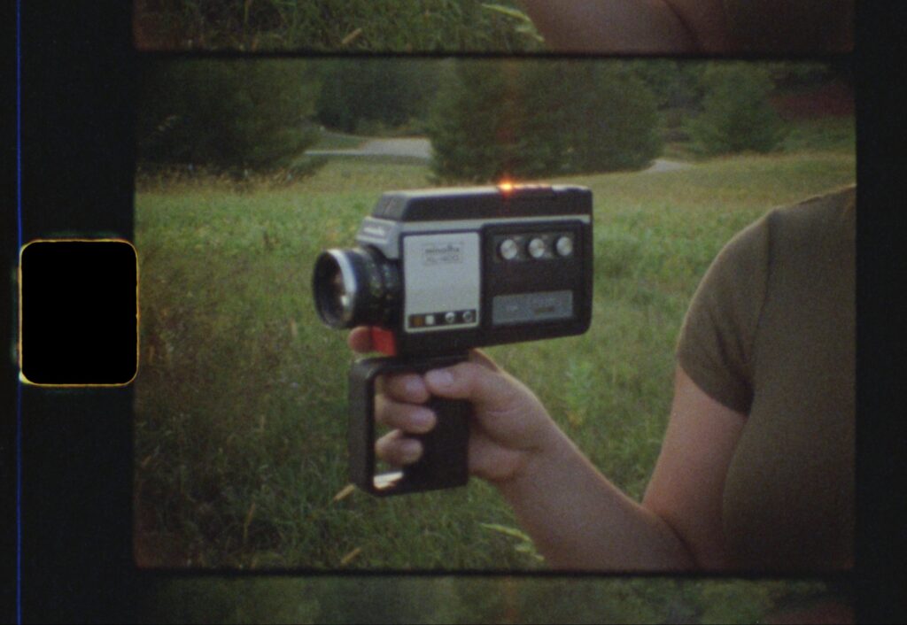 super 8 still image closeup of holding a super 8 film camera at sunset in a grassy field