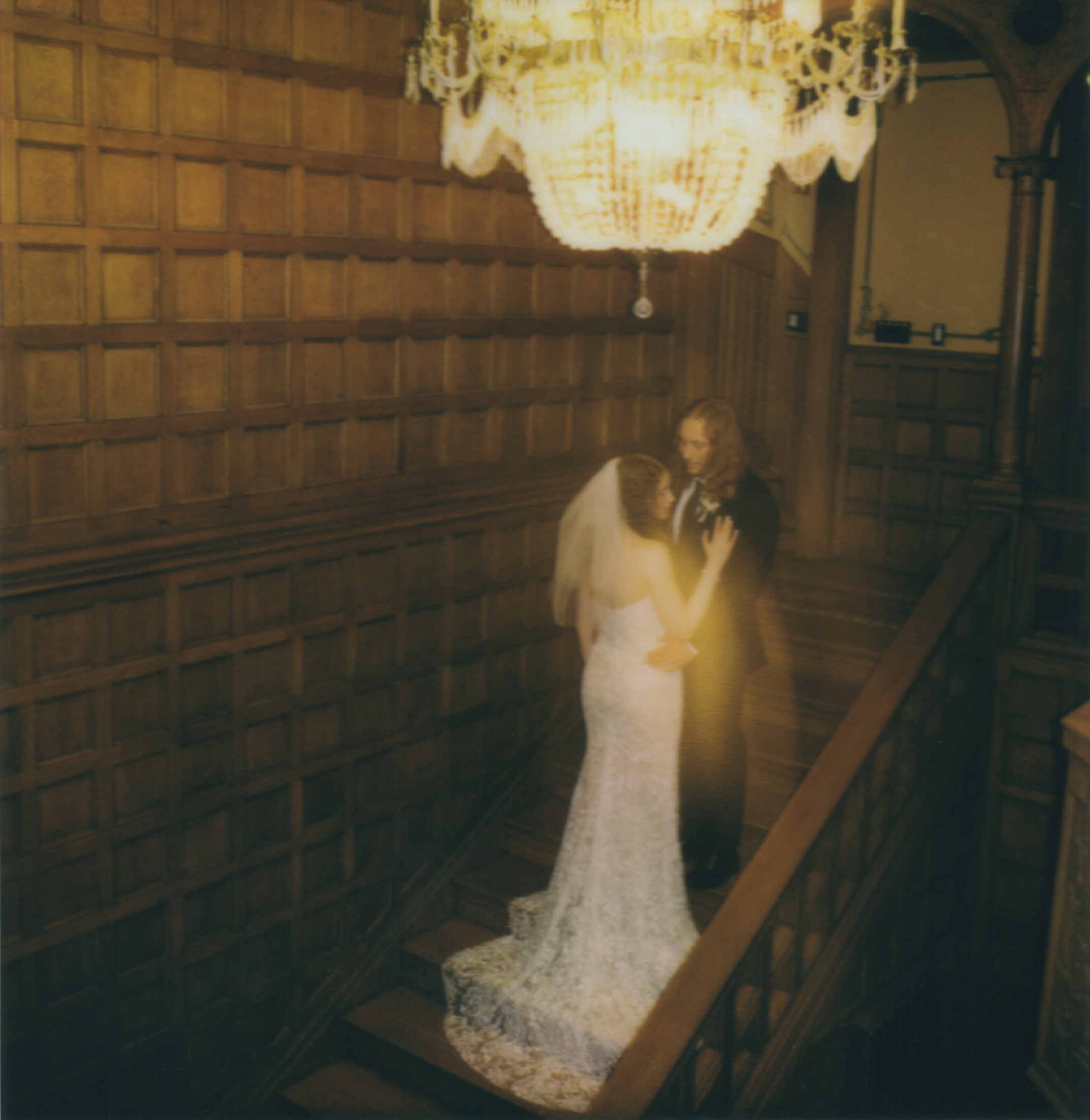 bride and groom under chandelier on stairs captured on polaroid film