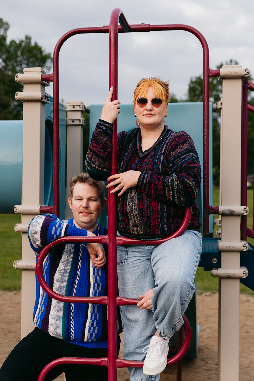 couple intertwining their legs on park playground for editorial 80s styled engagement photos in at a park in minnesota