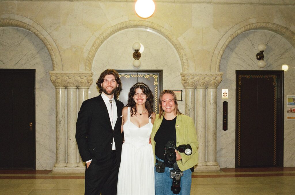 photographer brianna standing with newly wed couple with marble arches behind them