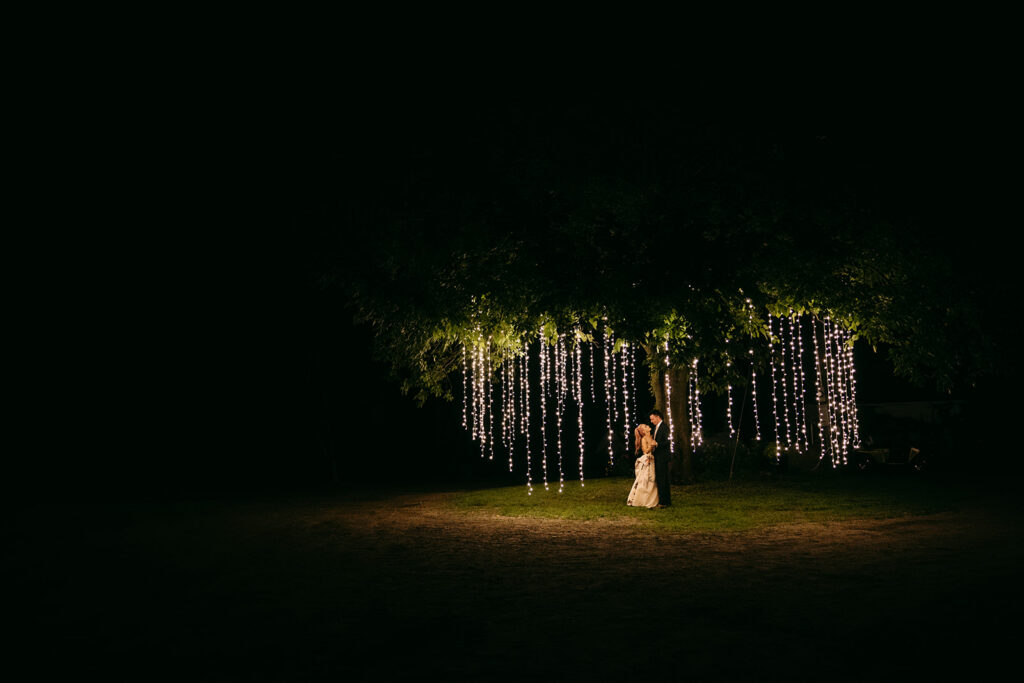 Bride and groom dancing under a oak tree with a led hanging light installation surrounding them in Minnesota. 